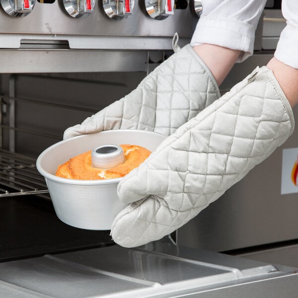A person wearing oven mitts holding a Chicago Metallic Angel Food Cake Pan full of food.