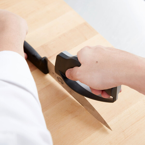 A hand using a Victorinox handheld knife sharpener to sharpen a knife on a counter.