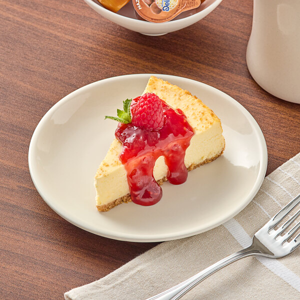 An Acopa ivory stoneware plate with a slice of cheesecake topped with raspberry sauce and a fork.