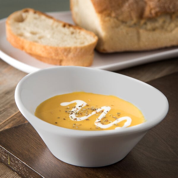 A Carlisle griege melamine bowl filled with soup on a table next to a loaf of bread.