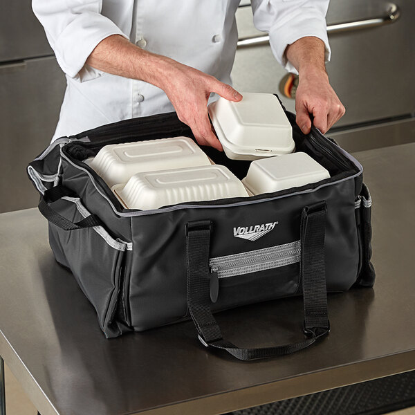 A person using a Vollrath 3-Series medium insulated food pan carrier bag to hold food containers.