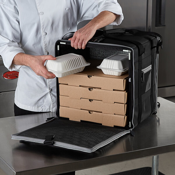 A person putting pizza boxes into a black zippered Vollrath delivery bag.