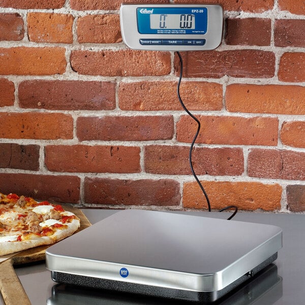 An Edlund digital pizza scale on a counter next to a pizza.