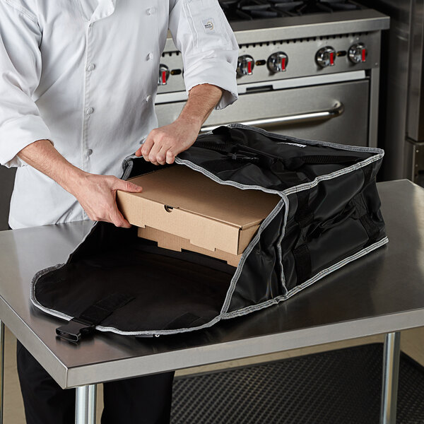 A chef putting a pizza in a Vollrath insulated delivery bag.
