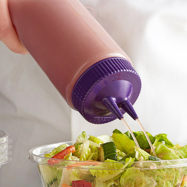 A hand using a Vollrath purple Twin Tip squeeze bottle to pour purple sauce onto a salad.