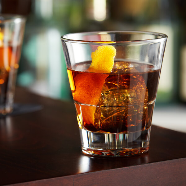 A Libbey stackable rocks glass filled with a brown drink and garnished with an orange peel.