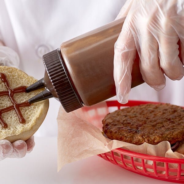 A person using a Vollrath brown Twin Tip squeeze bottle to put sauce on a hamburger.