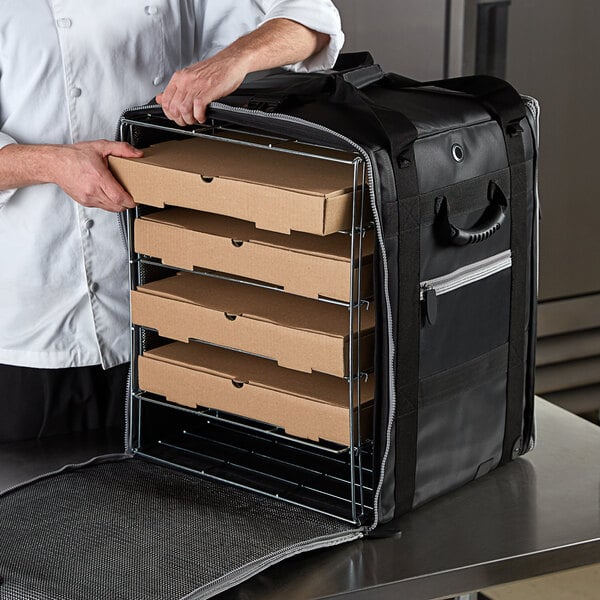 A person putting pizza boxes in a large Vollrath insulated tower bag with wire insert.