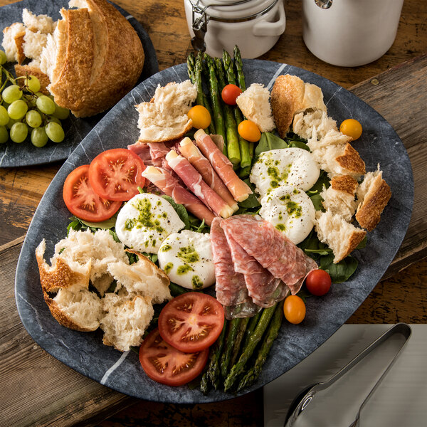 A Carlisle Ridge soapstone melamine platter with meat, vegetables, and bread on a table.