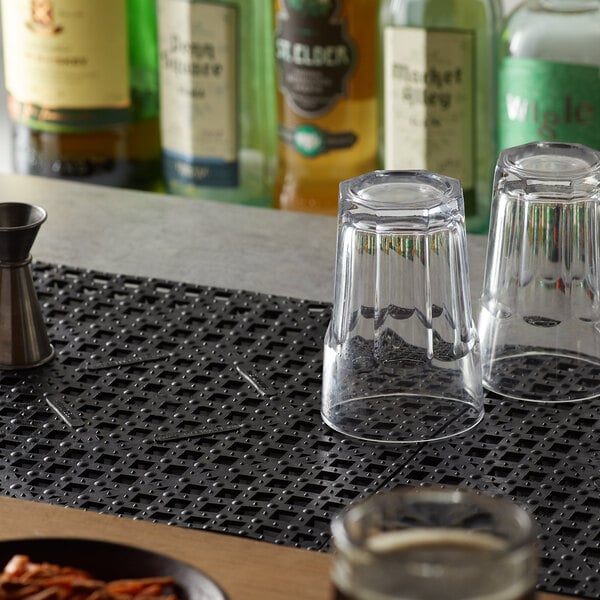 A black interlocking bar mat on a table with glasses and a bottle of liquor.