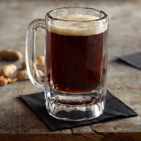 An Anchor Hocking glass mug of beer on a napkin next to peanuts.