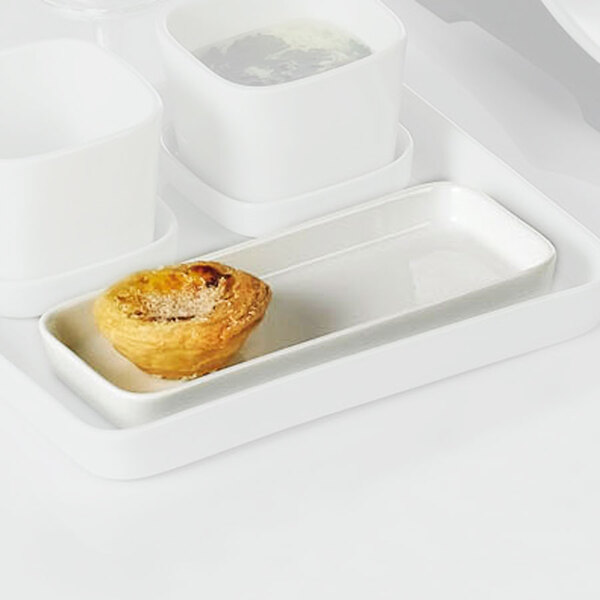 A white rectangular porcelain tasting tray with a pastry and white cup on it.