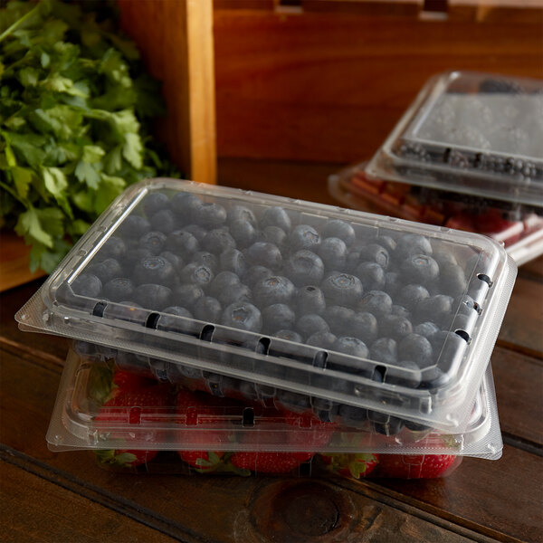 Three clear plastic vented containers of blueberries and blackberries on a counter.