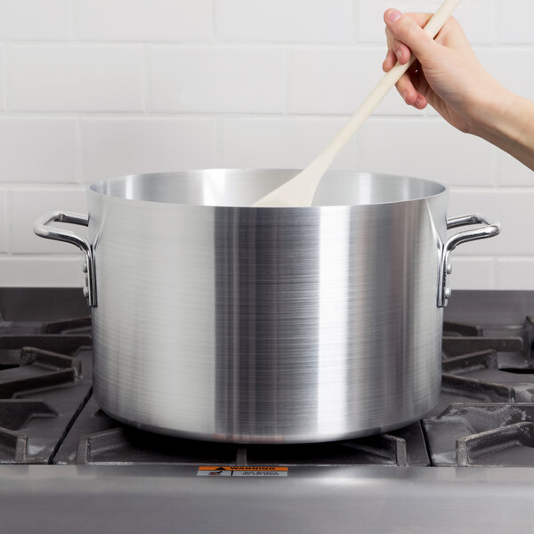 A hand stirring a Vollrath Arkadia sauce pot on a stove with a wooden spoon.