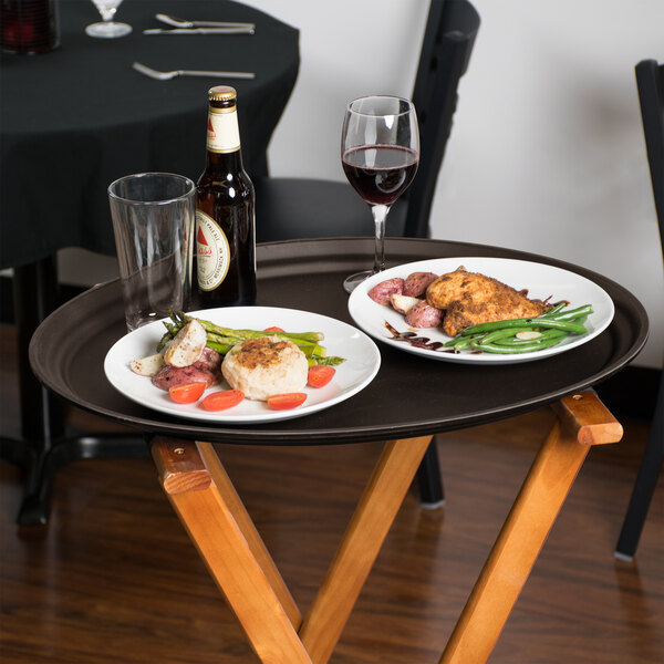 A Tavern Tan non-skid oval serving tray with a plate of food and a glass of wine on a table.
