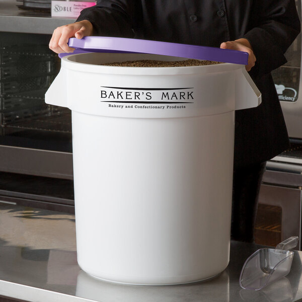 A woman holding a large white Baker's Mark ingredient storage container with a purple allergen-free lid.