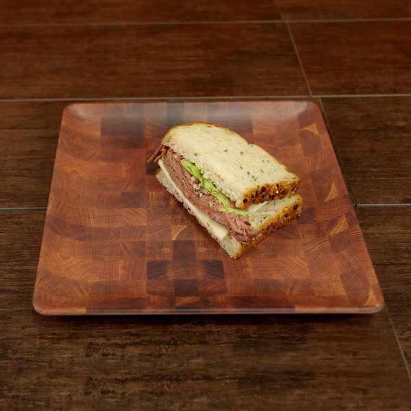 A sandwich with meat and lettuce on a square bamboo and melamine plate.