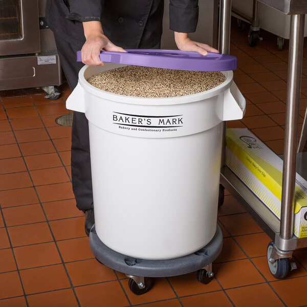 A woman standing in front of a large white Baker's Mark ingredient storage bin with a purple lid.