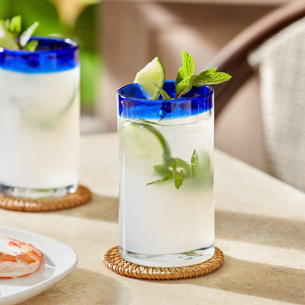 Two Acopa Tropic cooler glasses filled with water and garnished with lime and mint on a table.