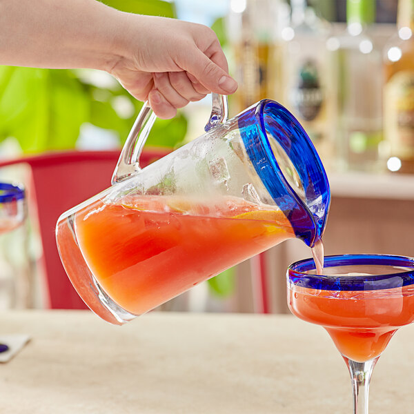 A person using an Acopa Tropic glass pitcher to pour a drink into a glass.