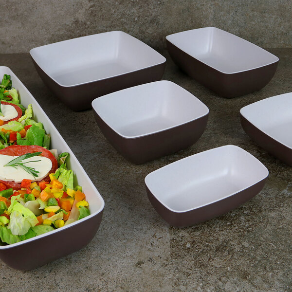 A white rectangular melamine bowl with a brown and white speckled interior holding a salad.