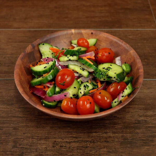 A round bamboo and melamine bowl filled with a salad of cucumbers, tomatoes, and onions.