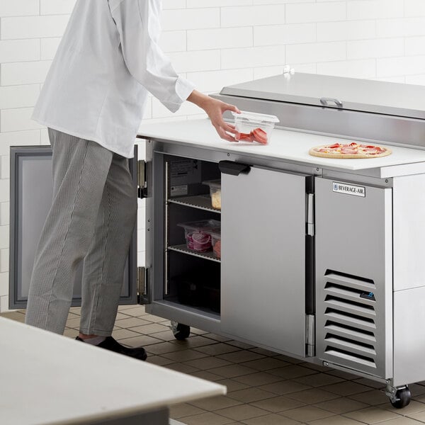 A man standing in front of a Beverage-Air 2 door pizza prep table in a school kitchen.