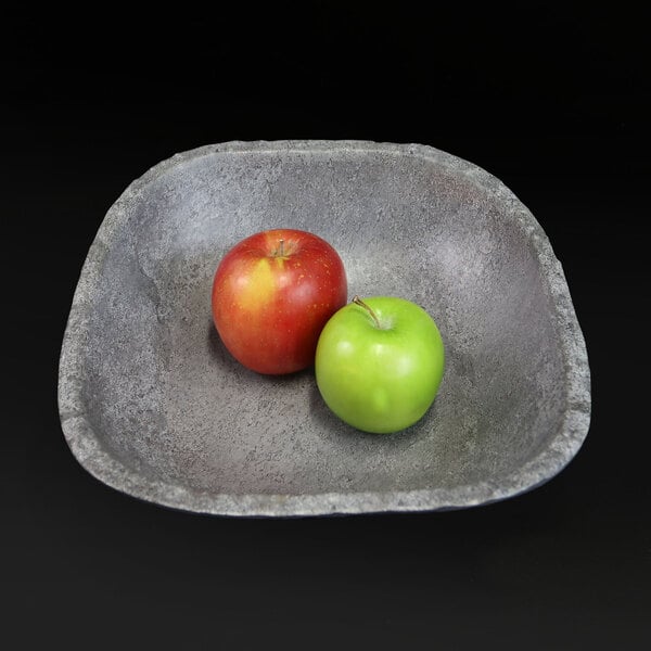 A rectangular coal colored stone bowl filled with a red and green apple.
