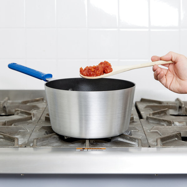 A person stirring food in a Vollrath Wear-Ever sauce pan with a blue silicone handle.