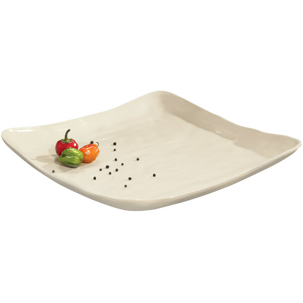 A white square melamine serving platter with food and an orange pepper on it.
