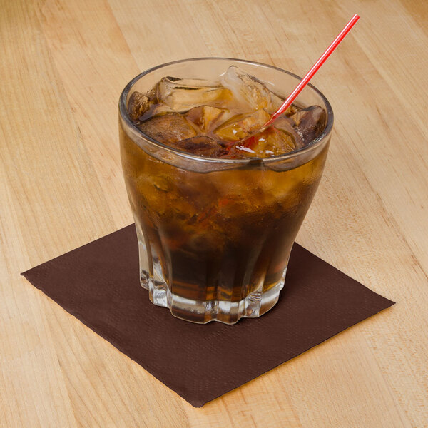 A glass with a brown cocktail napkin and a straw on a table.