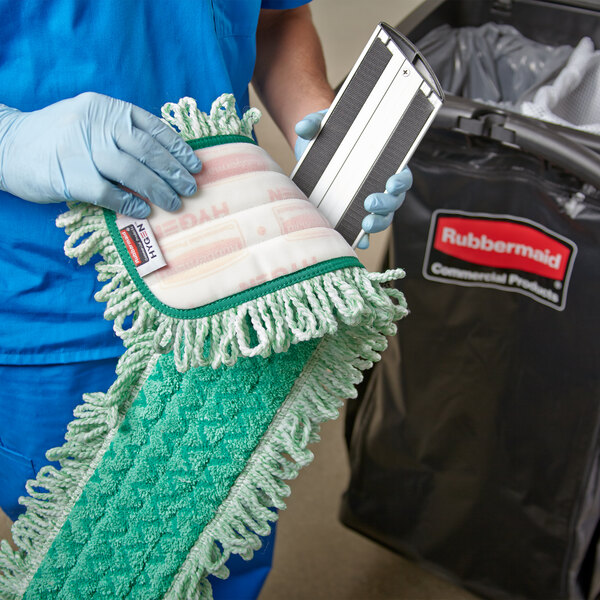 A person in blue scrubs using a green Rubbermaid microfiber fringed dust mop pad.