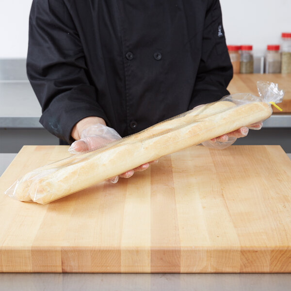 A person holding a baguette in a plastic bread bag.