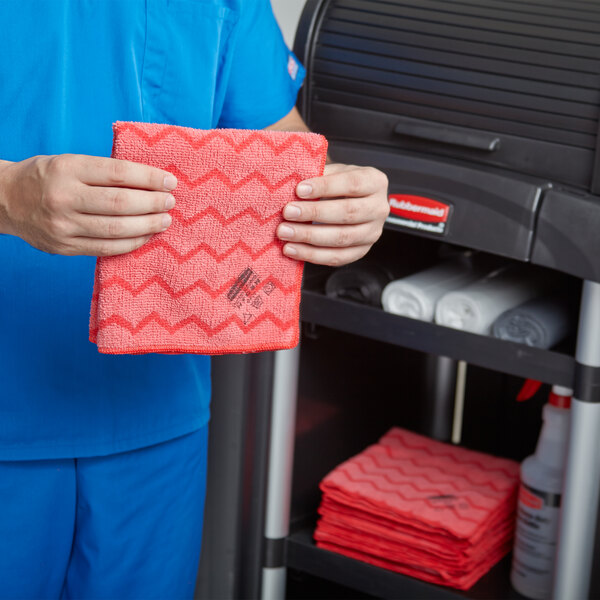 A man in blue scrubs using a red Rubbermaid HYGEN microfiber cloth on a counter.