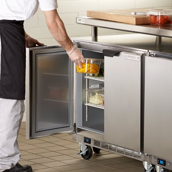 A person opening the door of a Beverage-Air undercounter refrigerator to get food.