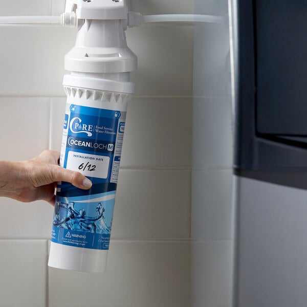 A hand holding a white C Pure Oceanloch-M water filter cartridge.