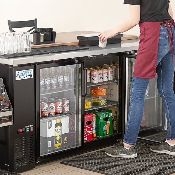 A woman standing at a counter with a beverage in a black Avantco back bar refrigerator.