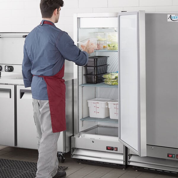 An Avantco reach-in refrigerator with a white door. A man in a red apron opens the door.
