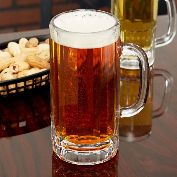 A Libbey glass mug of beer on a table with peanuts.