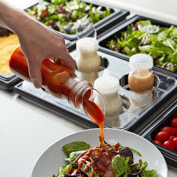 A person pouring clear sauce from a clear bottle onto a salad.