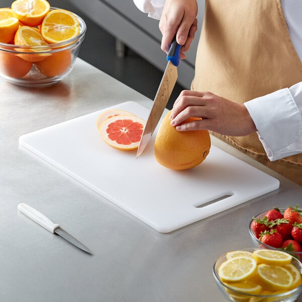 A person cutting an orange on a white polyethylene cutting board with a white handle.