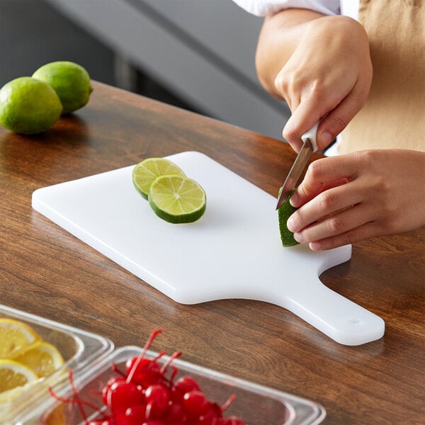 A person cutting limes on a Thunder Group white polyethylene cutting board with a handle.