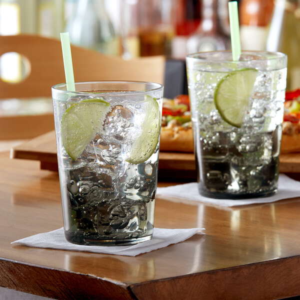 Two Arcoroc grey beverage glasses filled with water, ice, and lime slices on a table.