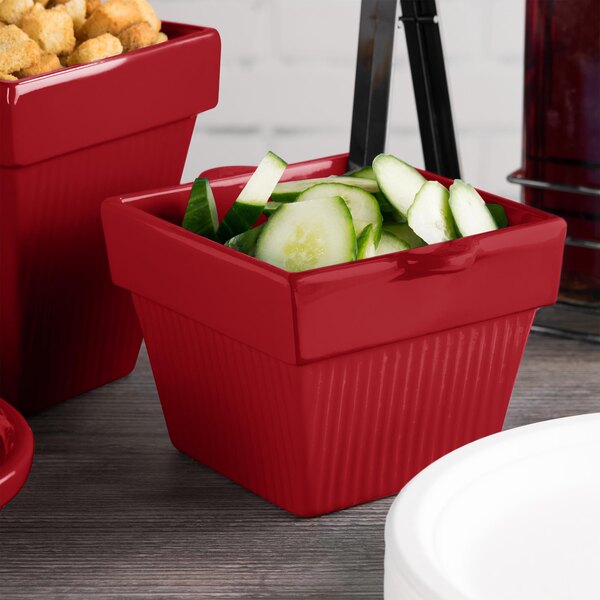 A red Tablecraft square condiment bowl with cucumbers in it.