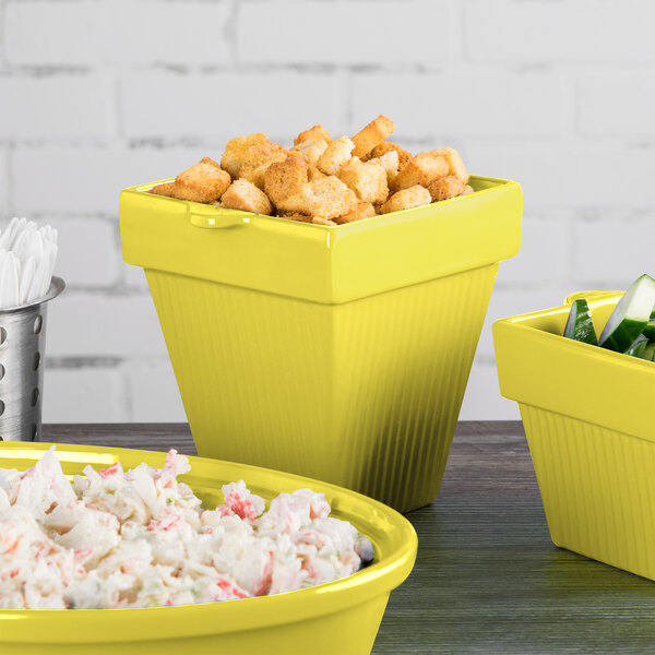 A group of Tablecraft yellow cast aluminum square condiment bowls filled with food on a counter.
