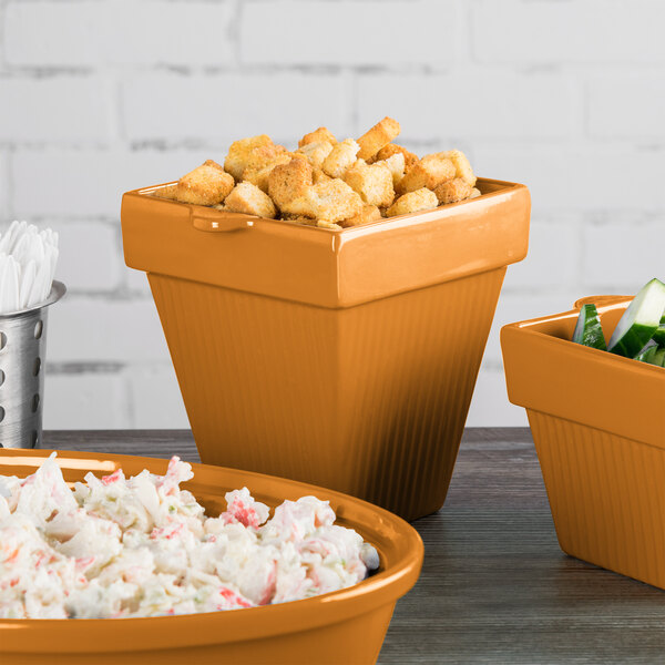 A Tablecraft orange square condiment bowl on a table with other bowls of food.