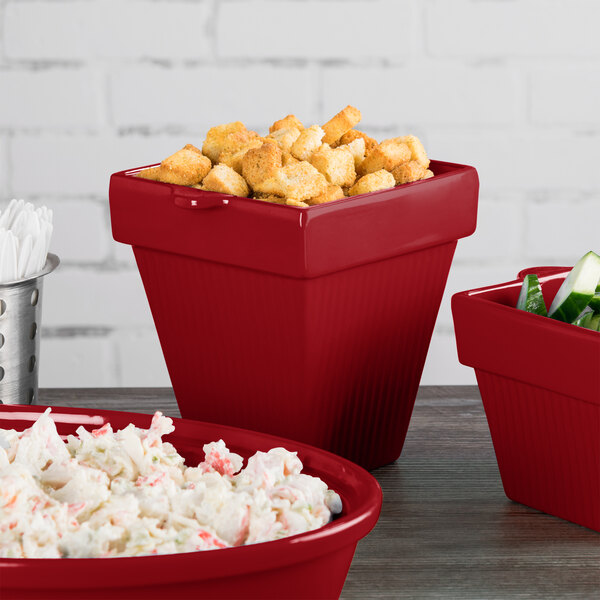 A group of Tablecraft red cast aluminum square condiment bowls with food in them.