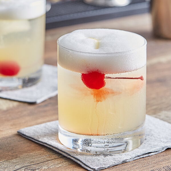 An Acopa Straight Up Rocks glass filled with liquid and a cherry on top on a wooden tray.