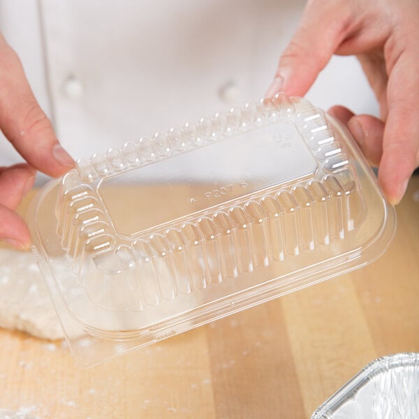 A person's hand placing a clear plastic dome lid on a plastic container of dough.