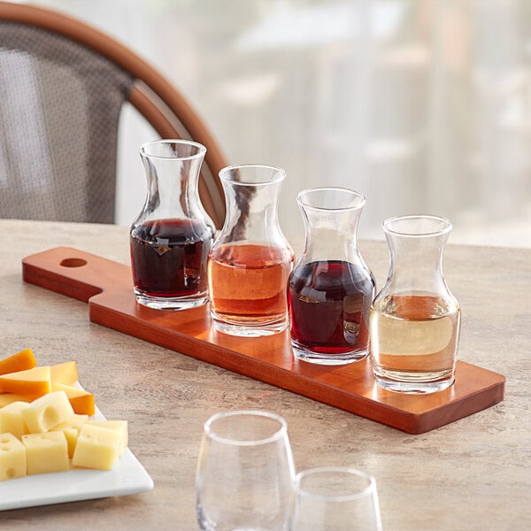 An Acopa wood flight paddle with glass carafes filled with different colored liquid on a table.